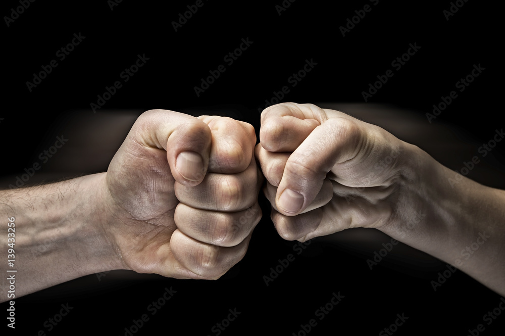 Image close up clash of two fists on black background. Concept of confrontation, competition etc.