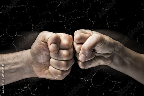 Image close up clash of two fists on black background with cracks. Concept of confrontation, competition etc. photo