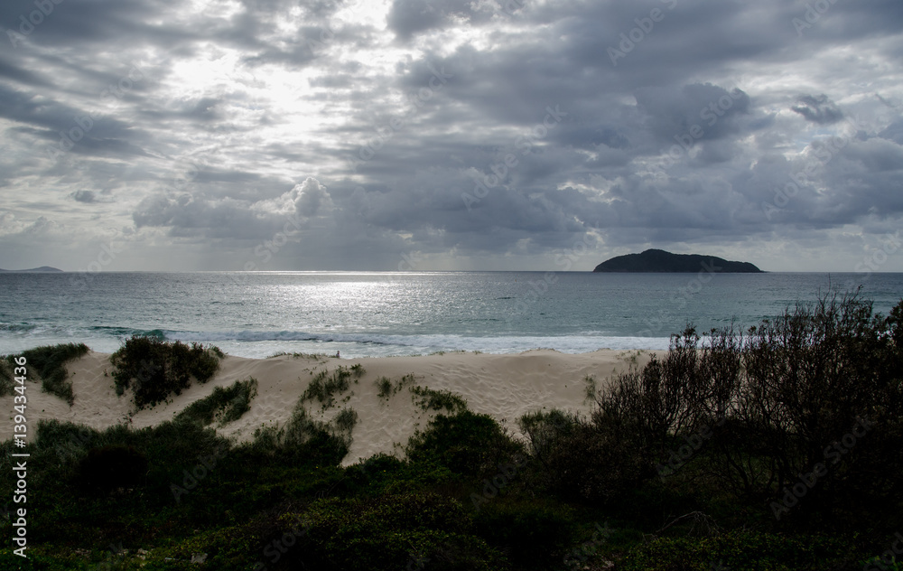 Sun breaking through storm clouds over remote beach and sand dunes