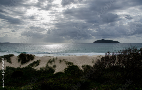 Sun breaking through storm clouds over remote beach and sand dunes © Ben R