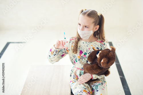 Little girl playing doctor at home, ready to make vaccination shot with medicine syringe to her toy teddy bear