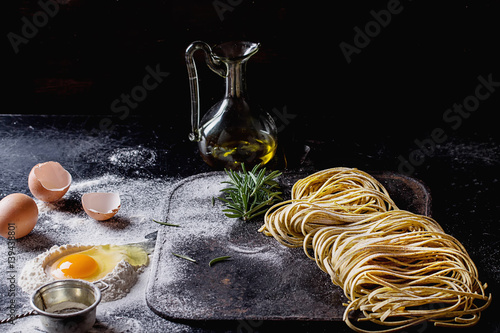 Raw uncooked black pepper spaghetti pasta with flour, egg rosemary, salt and spices and olive oil on vintage metal board over dark background. Space for text. photo