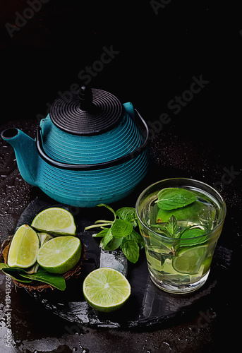 LimeIce tea  with  chinese tea pot mint, lime leaves and ice served in glasses on slate board. Dark Rustic Style photo