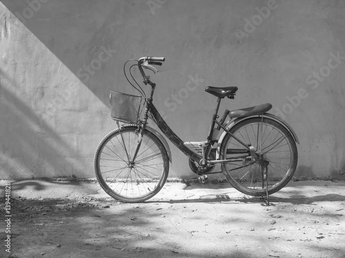 Vintage old bicycle standing against white concrete wall background with morning sunlight.