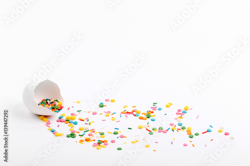 Egg shell colorful sugar sprinkle dots on white table with copy space. Easter concept