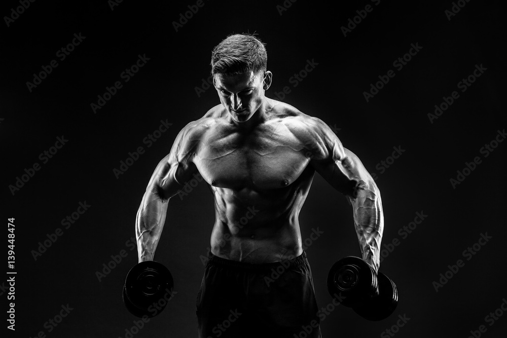 Handsome bodybuilder doing exercise with dumbbell. Studio shot. Black and white photo.