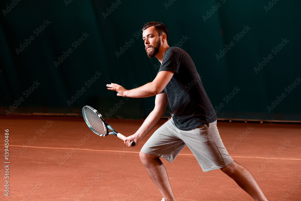 Handsome young man in t-shirt holding tennis racket on tennis court