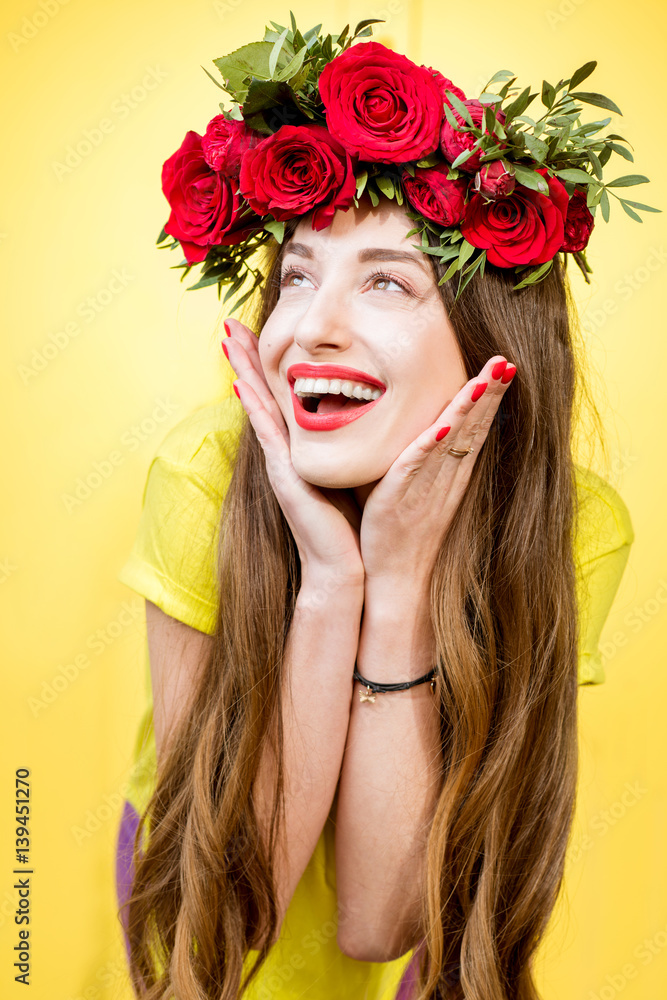 Naklejka premium Colorful portrait of a beautiful woman in yellow t-shirt with wreath made of red roses on the yellow background
