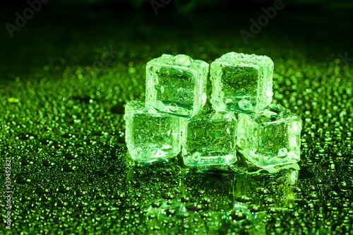 Ice cubes in green light on black wet table.