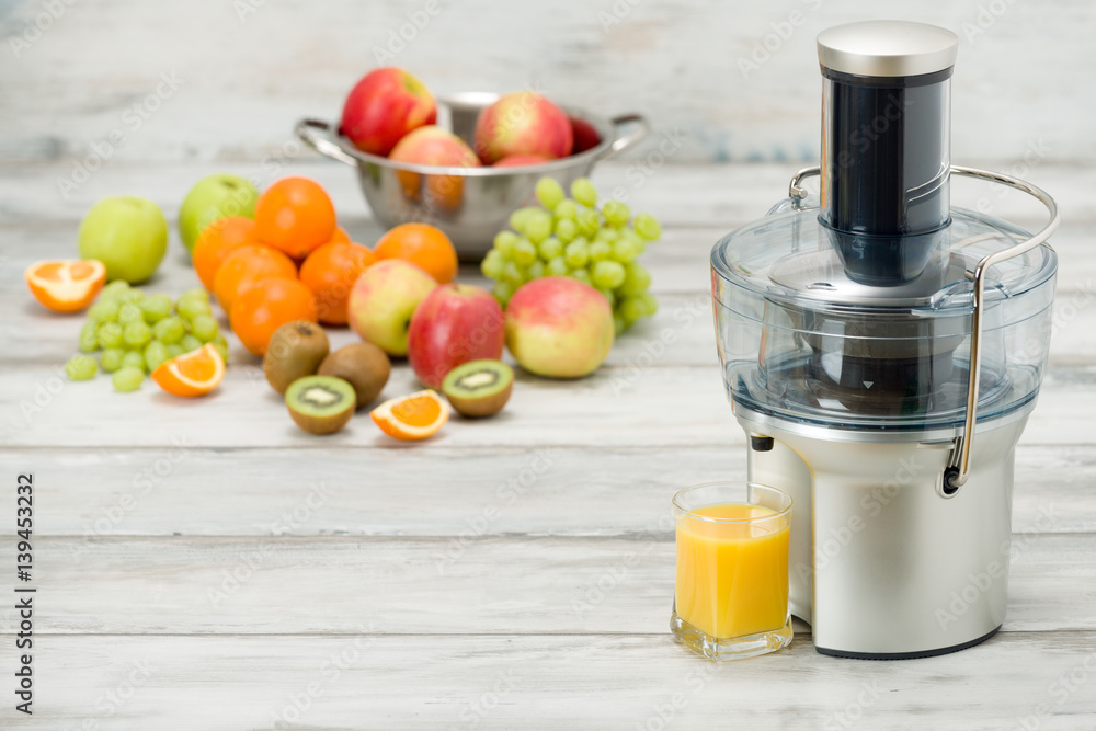 Modern electric juicer, various fruit and glass of freshly made juice, healthy lifestyle concept Modern electric juicer, various fruit and glass of freshly made juice, healthy lifestyle concept