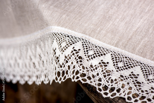 Macro shot of a linen tablecloth with white lace trim on a wooden table

 photo