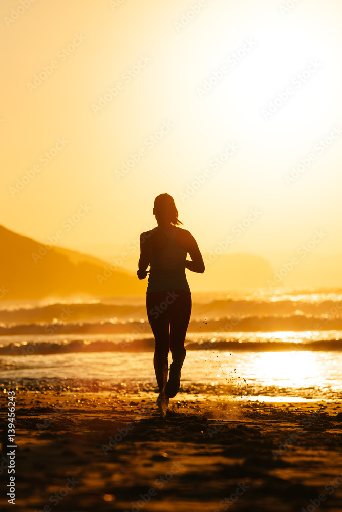 Silhouette of woman running on summer sunset at the beach towards the sun. Healthy exercise and lifestyle.
