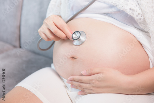 pregnant woman using stethoscope sitting on sofa close up