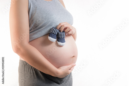 Pregnant woman holding small baby shoes on white background