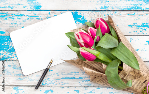 Fototapeta Naklejka Na Ścianę i Meble -  Bouquet tulips with empty sheet and pen on the old wooden background. Greeting card for women's day.