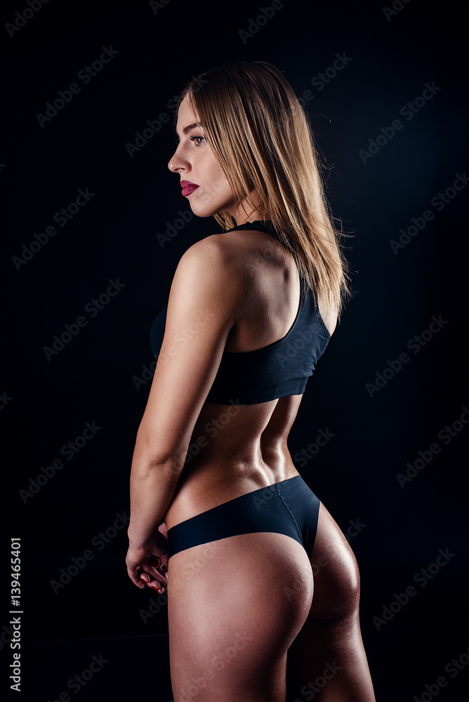 Sporty girl with great muscles in black sportswear. Tanned young athletic woman. A great sport female body. Muscular build female after workout.
