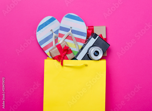 cute gifts, camera and cool sandals in shopping bag and cool laptop on wonderful pink background photo