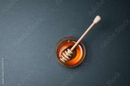 Small glass bowl of natural honey with stick. On the black stone rustic table.