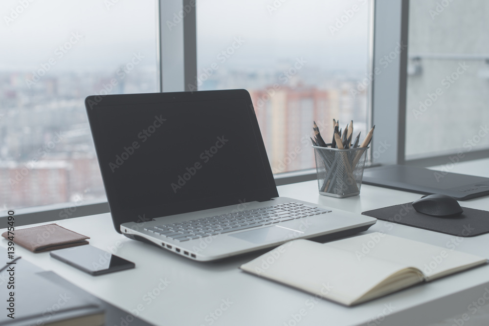 Fototapeta premium Workplace with notebook laptop Comfortable work table in office windows and city view.