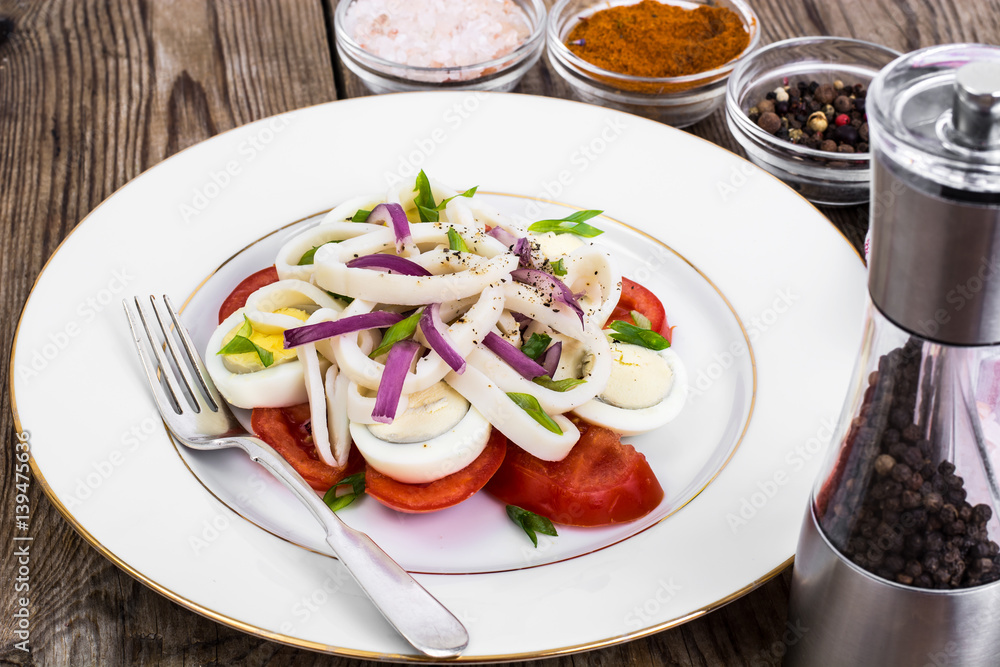 Salad with squid, egg and tomato on white plate on background of Salad with squid, egg and tomato on white plate on background of