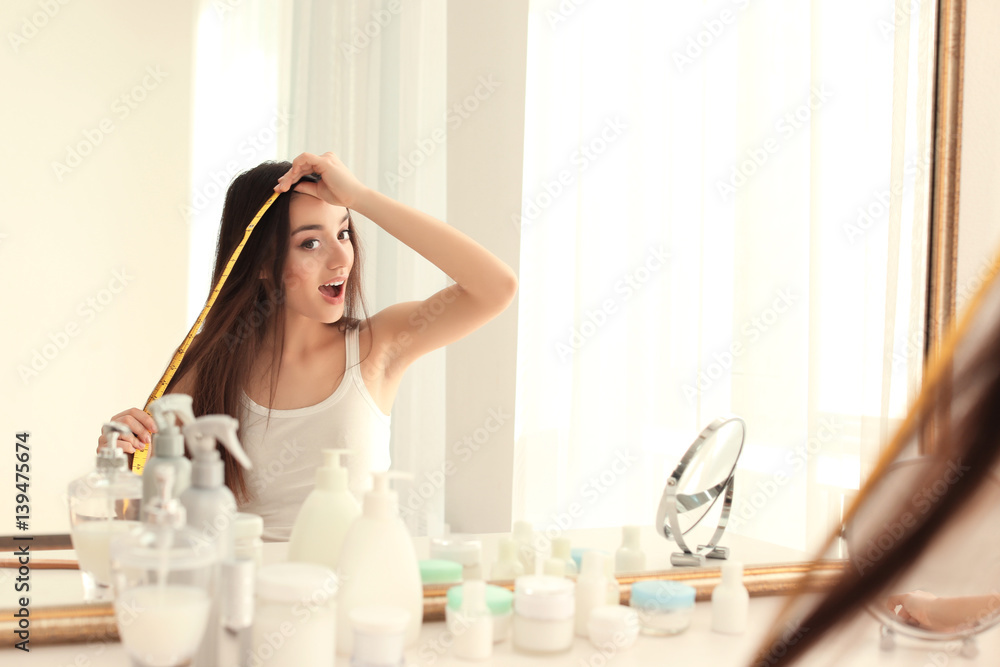 Young woman measuring hair length in front of mirror at home Young woman measuring hair length in front of mirror at home
