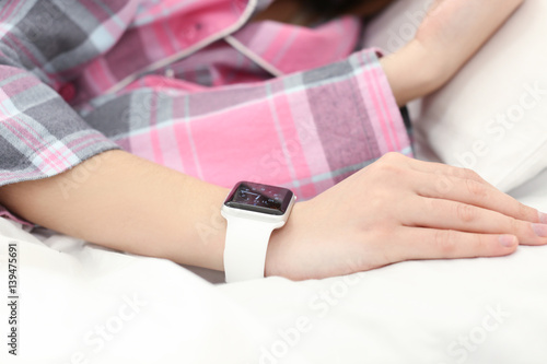 Hand of young woman with sleep tracker resting in bed at home