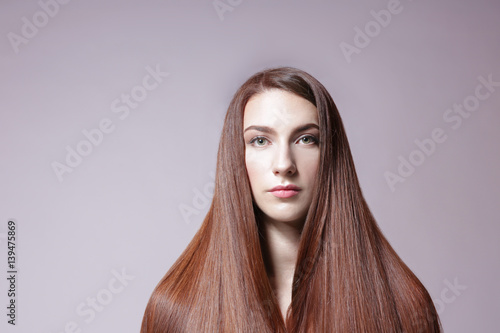 Beautiful young woman with long straight hair on light background