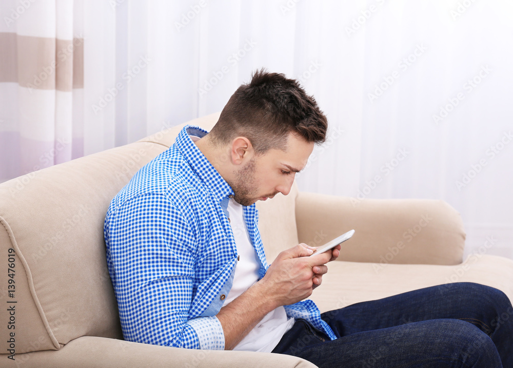 Handsome young man sitting on sofa at home. Incorrect posture concept Handsome young man sitting on sofa at home. Incorrect posture concept