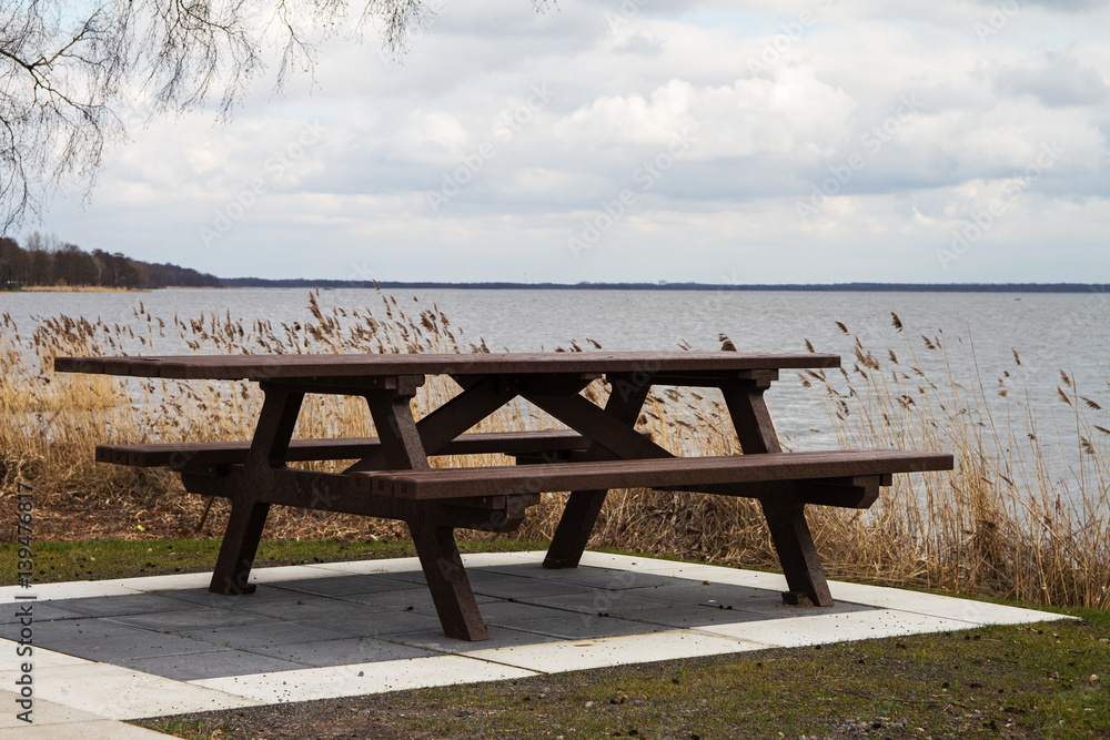 Hölzerne Sitzbank mit Tisch am Ufer eines Binnensee Hölzerne Sitzbank mit Tisch am Ufer eines Binnensee