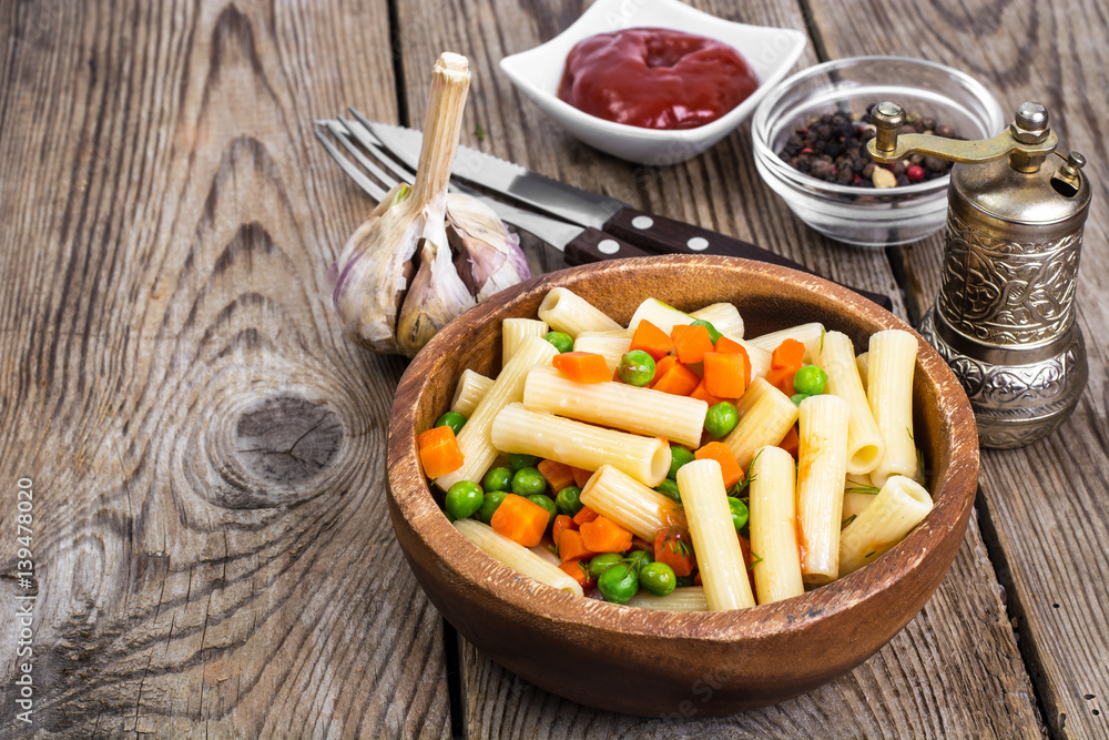 Pasta with carrots and green peas in wooden bowl