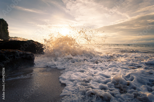 Ocean wave with foam beating against the rocks at sunset