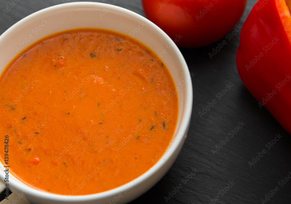 Cream soup with roasted peppers and tomatoes on black plate