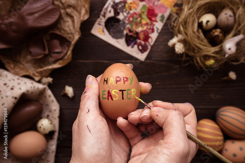 Happy easter. Female hands painting easter egg on the wooden table.
