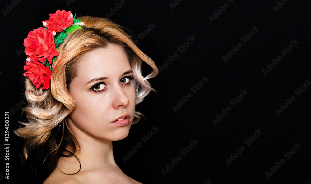 Woman with blonde laying and rimmed with red flowers on a dark background smiling. Close-up. Space for text