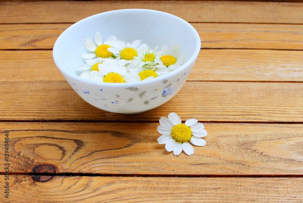 Chamomile flowers in a white plate on a wooden table Chamomile flowers in a white plate on a wooden table