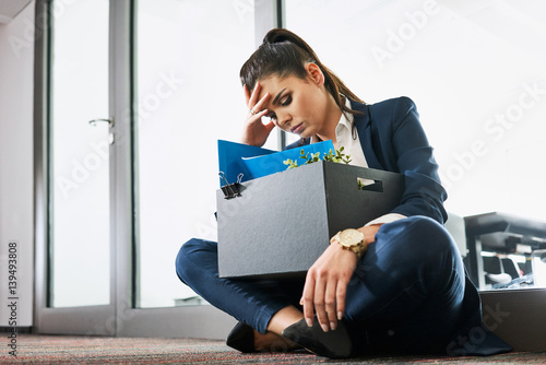 Fired young woman, employee sitting with box outside the office