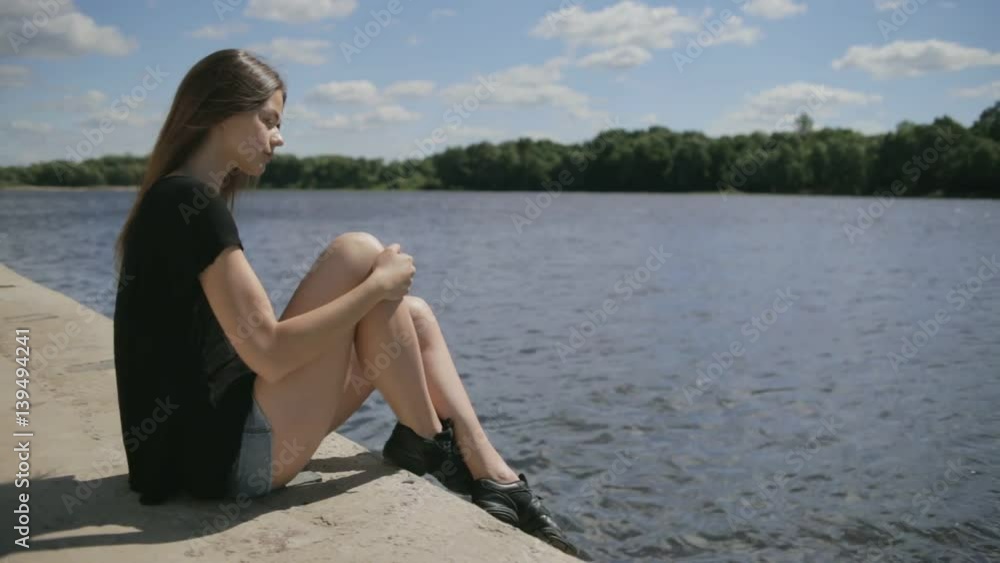 Young pretty woman sitting near river looking at river