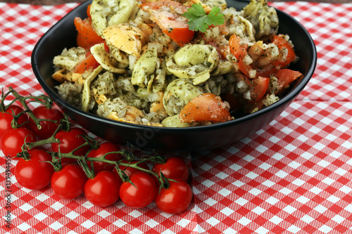 Bowl of tricolor tortellini pasta salad with tomatoes and onions on dark wood table background