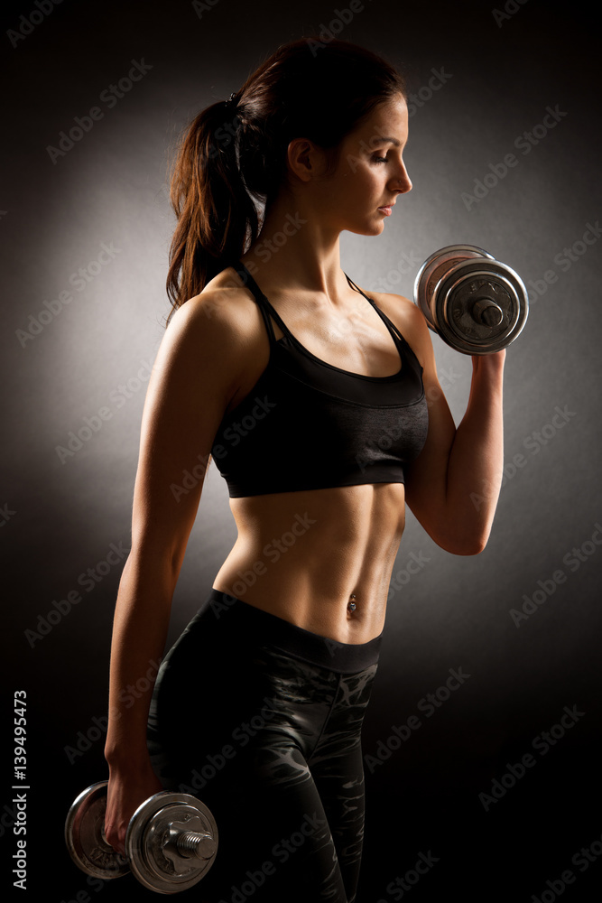 Atractive fit woman works out with dumbbells as a fitness conceptual over dark background Atractive fit woman works out with dumbbells as a fitness conceptual over dark background