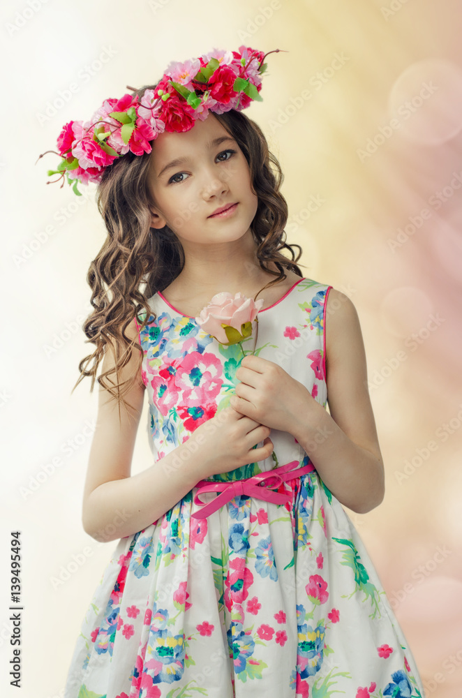 Portrait of cute little girl in nice spring dress, with flower wreath on head, holds pink rose in hands. Portrait of cute little girl in nice spring dress, with flower wreath on head, holds pink rose in hands.