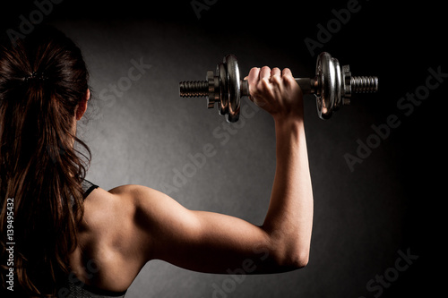 Fototapeta Naklejka Na Ścianę i Meble -  Atractive fit woman works out with dumbbells as a fitness conceptual over dark background