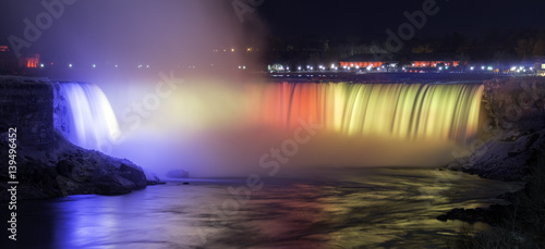The Canadian Niagara Falls beautifully illuminated at night in blue, red and yellow, winter tourism scene