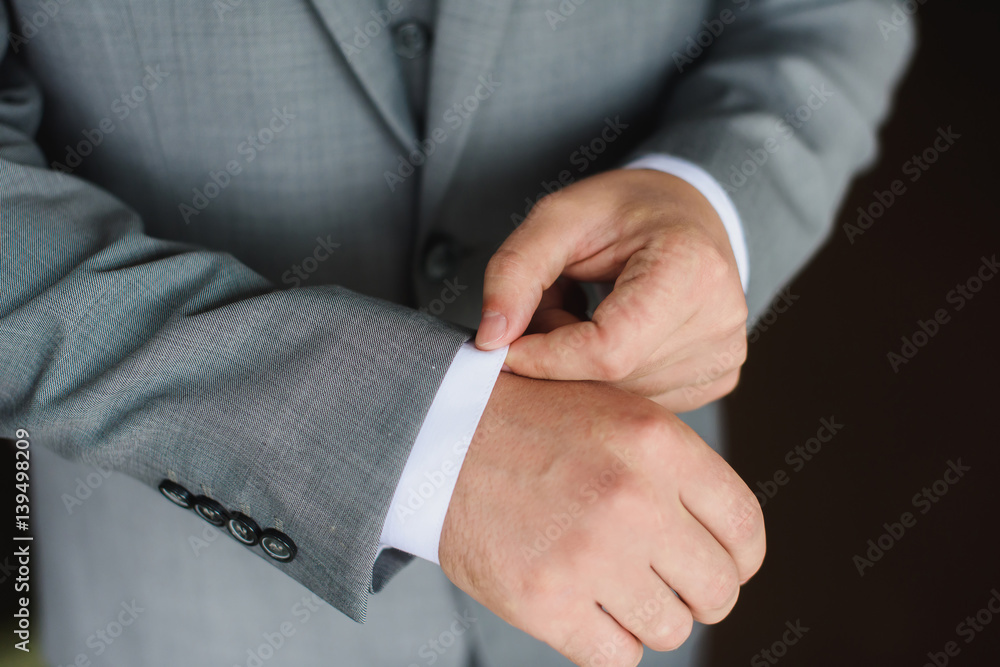 Elegant young fashion man dressing up for wedding celebration. Color close up image of male hands. Groom buttoning a shirt. Dark background.