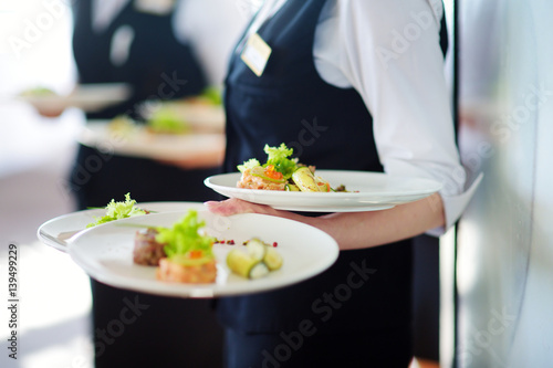 Waiter carrying plates with meat dish on some festive event photo