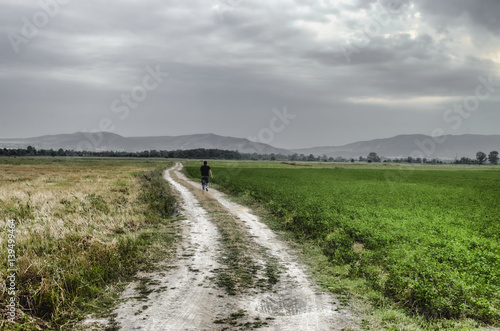Pathway up the hill against the sky. Man ran away. Man walking on road. Field with green and yellow grass. Azerbaijan