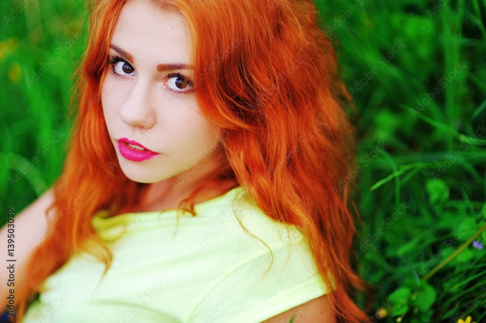 Portrait of a cute red-haired girl with beautiful brown eyes, resting on a green lawn in a Park, closeup. Portrait of a cute red-haired girl with beautiful brown eyes, resting on a green lawn in a Park, closeup.