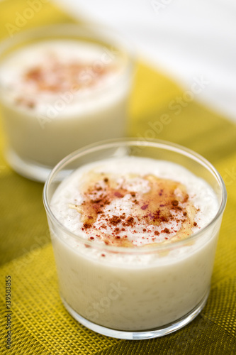 Pudding With Maple Syrup Drizzle & Cinnamon. Coconut flavored rice pudding dessert with maple syrup drizzle on top and sprinkled cinnamon served in glass bowl. Portrait orientation.