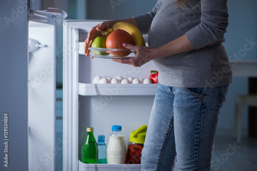 Pregnant woman near fridge looking for food and snacks at night