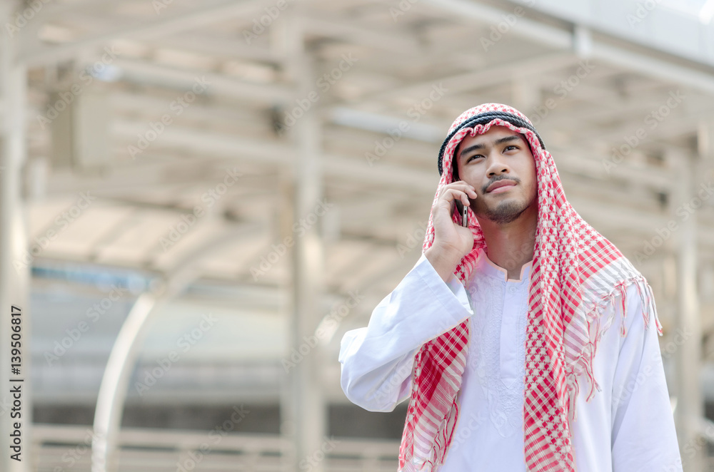 Fototapeta premium Young Arab businessman using mobile phone while walking in the city.