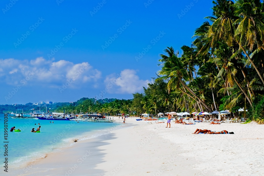 Beautiful tropical white sand beach with coconut palms and people on the beach